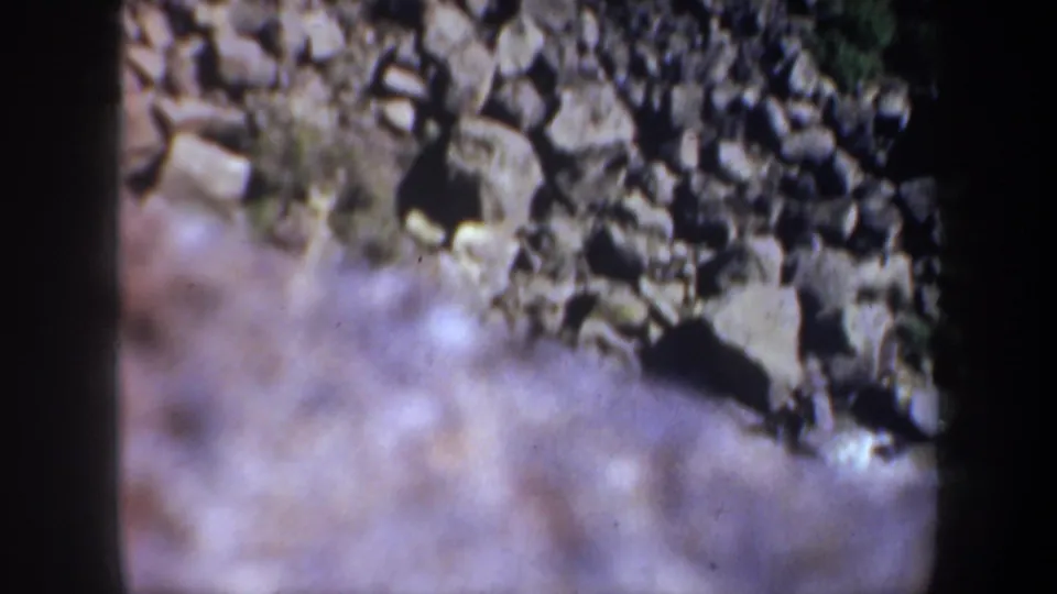 1957 Oregon 8mm frame with a rocky slope at the top and soft, pale river water moving through the lower foreground.