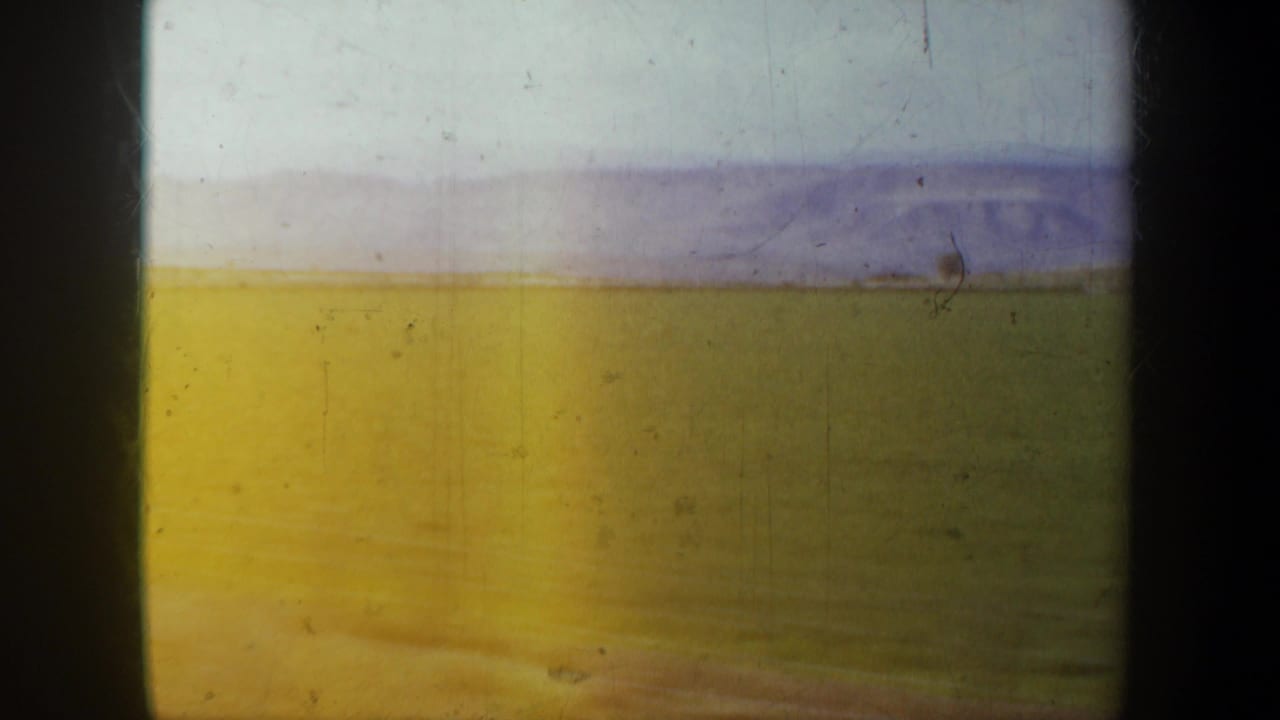 1957 Oregon 8mm view from a moving vehicle across an open field toward distant low mountains under a pale sky.