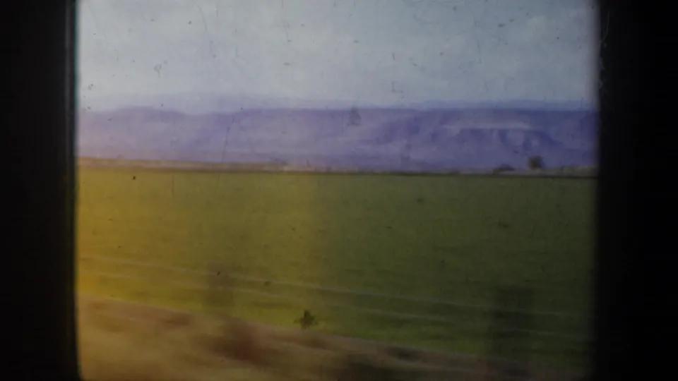 1957 Oregon home-movie frame showing green and brown fields receding toward distant hills beneath a bright sky.