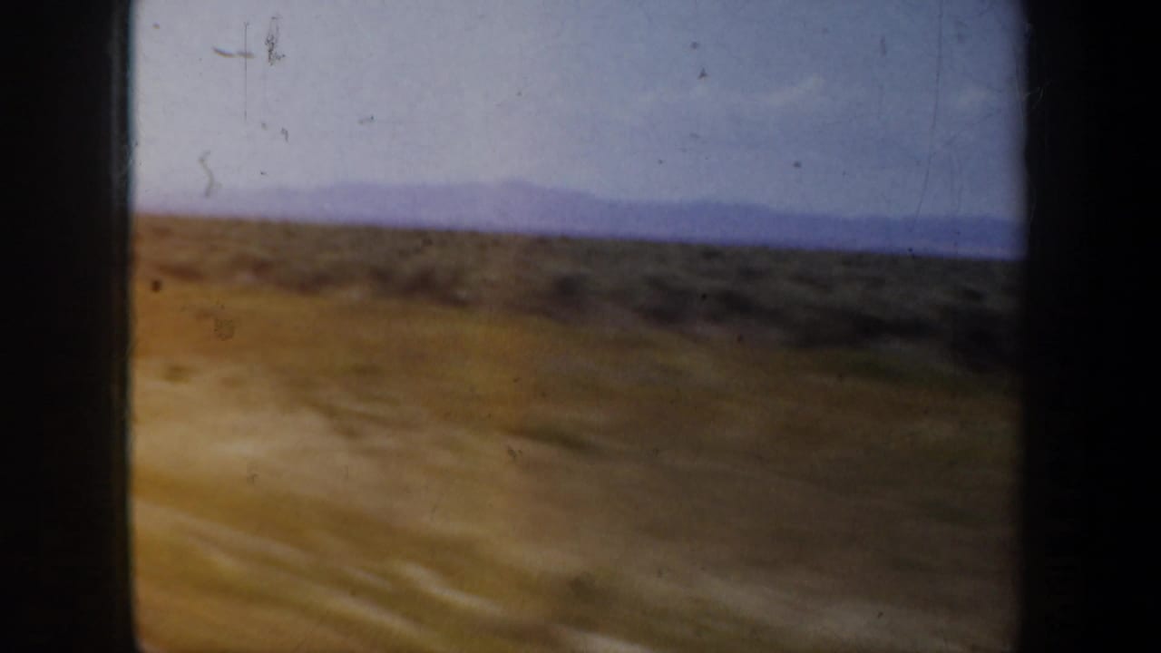 Dusty road edge and scrub terrain passing beneath distant mountains.