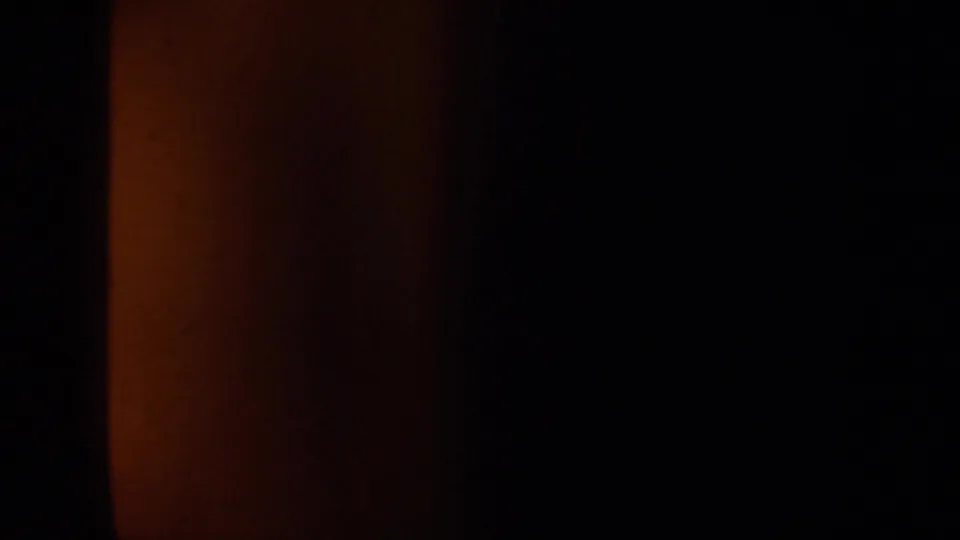 A transitional 8mm frame dominated by dark window or vehicle framing, with reddish exposure at the left edge and little landscape detail visible.