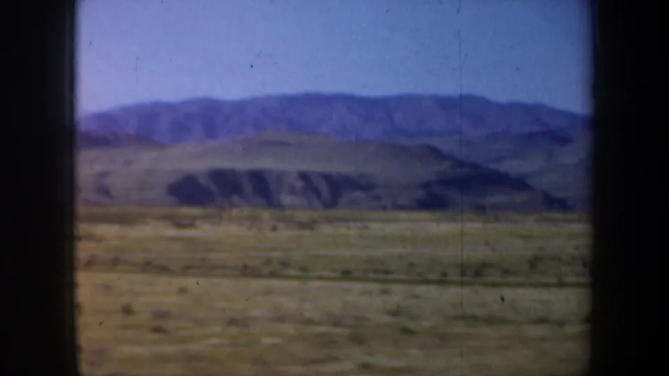 1957 Oregon home-movie frame showing open scrubland, rolling hills, and distant mountains from a moving vehicle.