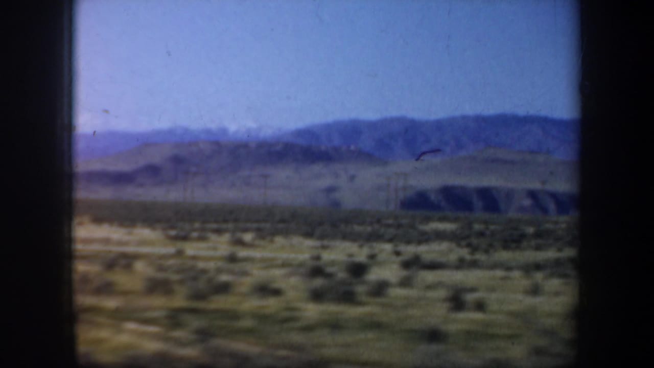 Wide rural terrain with hills and mountains viewed from a moving vehicle.