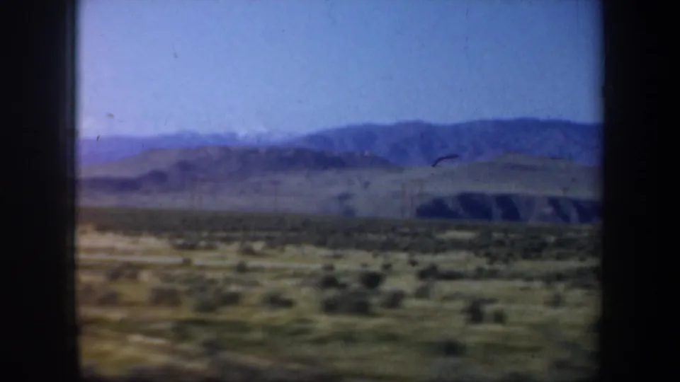 1957 Oregon travel view of broad dry terrain, low hills, and blue mountain ridges from a passenger perspective.