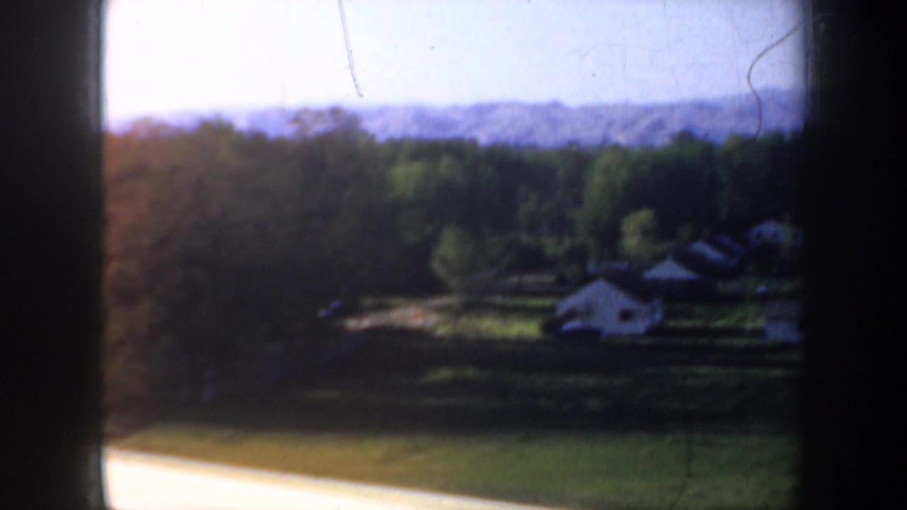 Rural fields and small houses seen through a dark car window frame.