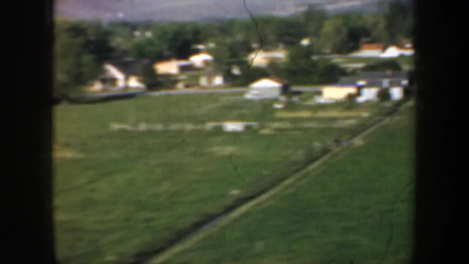 Rural Oregon fields and scattered farm buildings are seen from a car window during a brief 1957 countryside drive.
