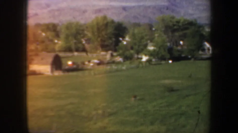 A grassy Oregon field with a small barn-like structure, nearby houses, trees, and low hills closes the moving road-view sequence.