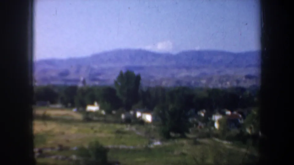 1957 Oregon home-movie still showing a soft-focus valley scene with trees, rural homes, pasture, and blue hills beyond.