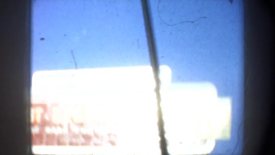 Near the end of the 1957 drive-by, the roadside signs fill the frame with strong overexposure and a windshield pillar crossing the view.