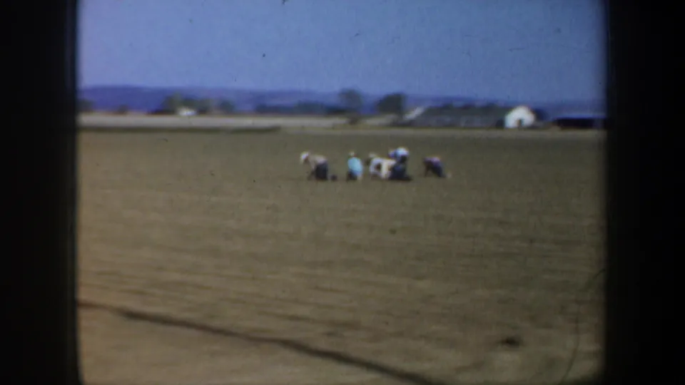 The Oregon 1957 frame shows distant people kneeling in a dry field, with a small structure and low hills across the horizon.