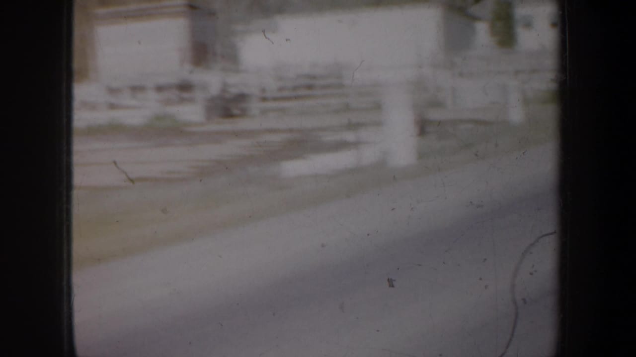 Blurred roadside view through a car window with pale fencing and a light building.