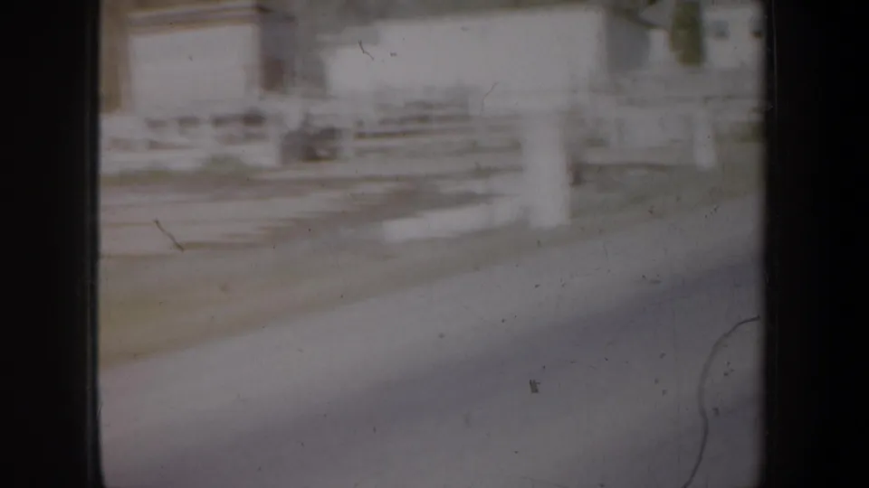 1957 Oregon home-movie frame showing a blurred roadside fence and light rural building seen through a dusty moving car window.