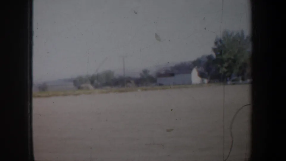 1957 Oregon 8mm view across open rural land toward trees and a pale farm building, with heavy gate borders and soft focus.