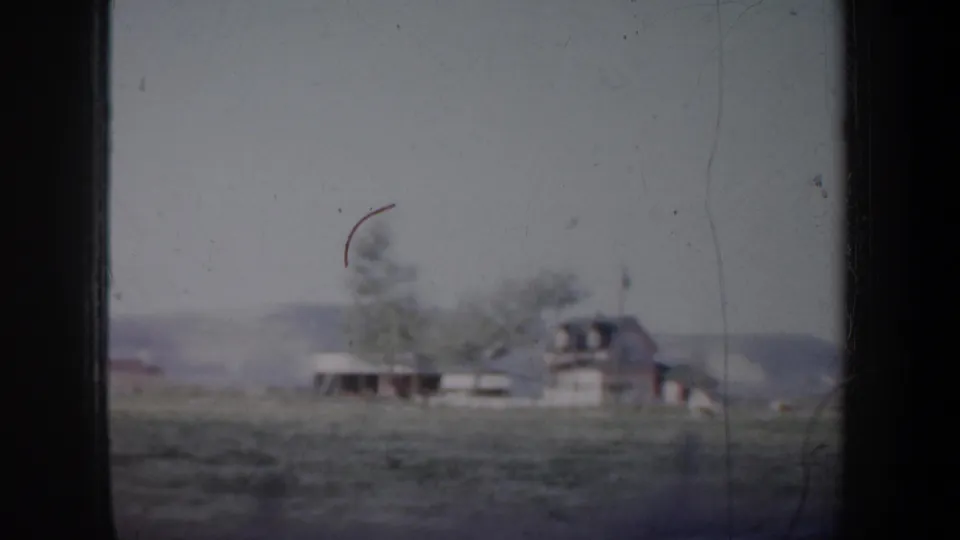 1957 Oregon 8mm frame showing a distant rural farmhouse with trees and fields under a pale sky.