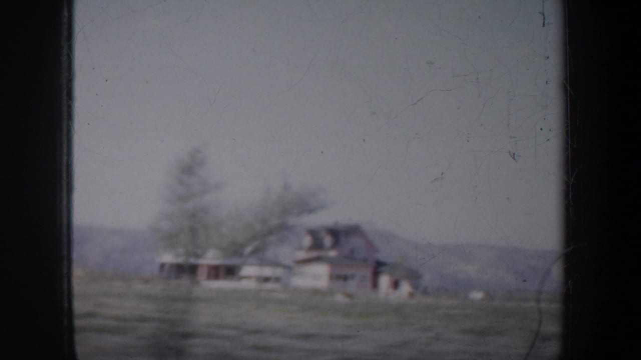 Soft view of a farmhouse, trees, field, and low hills through film-frame borders.