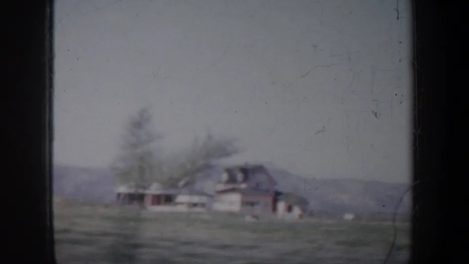 1957 Oregon countryside view with a distant house, trees, fields, and low hills in soft 8mm focus.