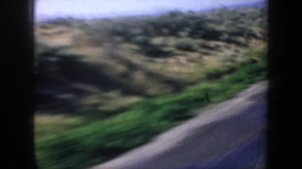 1957 Oregon roadside landscape with green verge, rolling scrubland, and motion blur from a moving vehicle.
