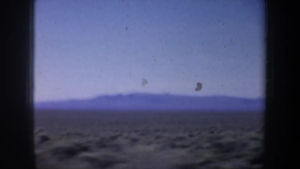 1957 Oregon 8mm frame with open brown fields and a distant mountain or hill silhouette under hazy blue sky.