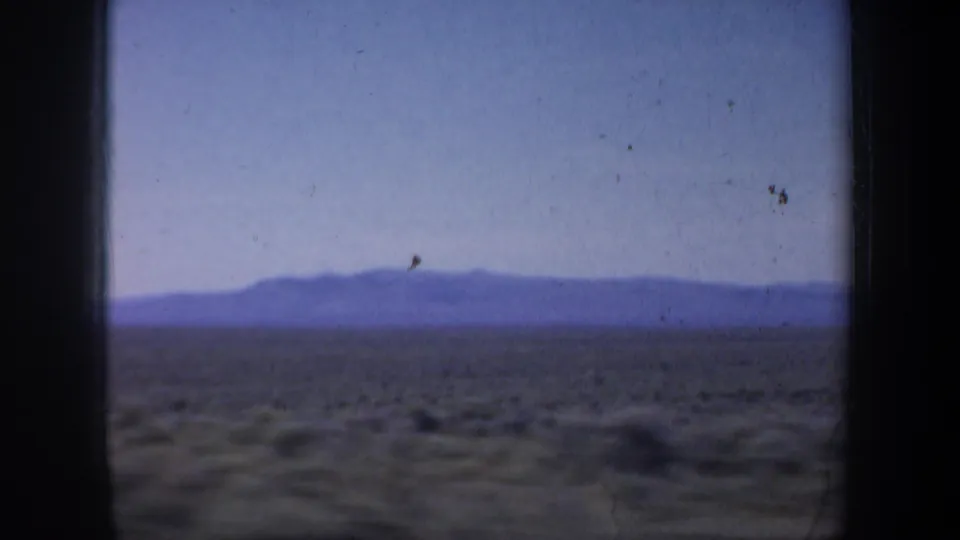 1957 Oregon 8mm frame showing open fields, a low distant mountain silhouette, and pale blue sky from a moving viewpoint.