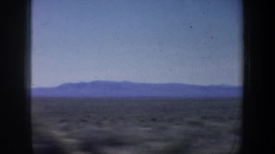 1957 Oregon 8mm frame with brown open land, distant hills or mountains, and clear blue sky seen through film borders.