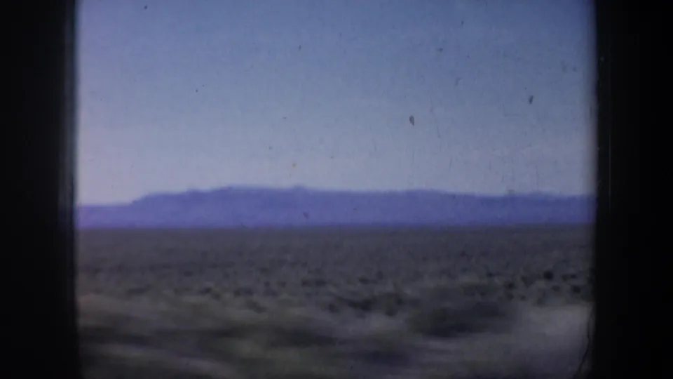 1957 Oregon 8mm view of low shrubs across an arid plain, with hazy hills on the horizon and dark film edges.
