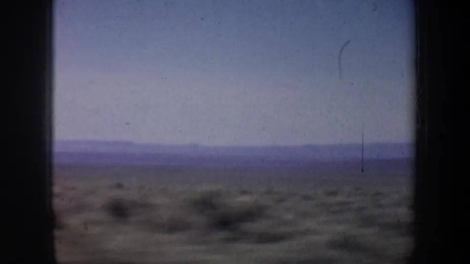 1957 Oregon home-movie frame showing blurred shrubs and a distant mountain line from a moving vehicle.