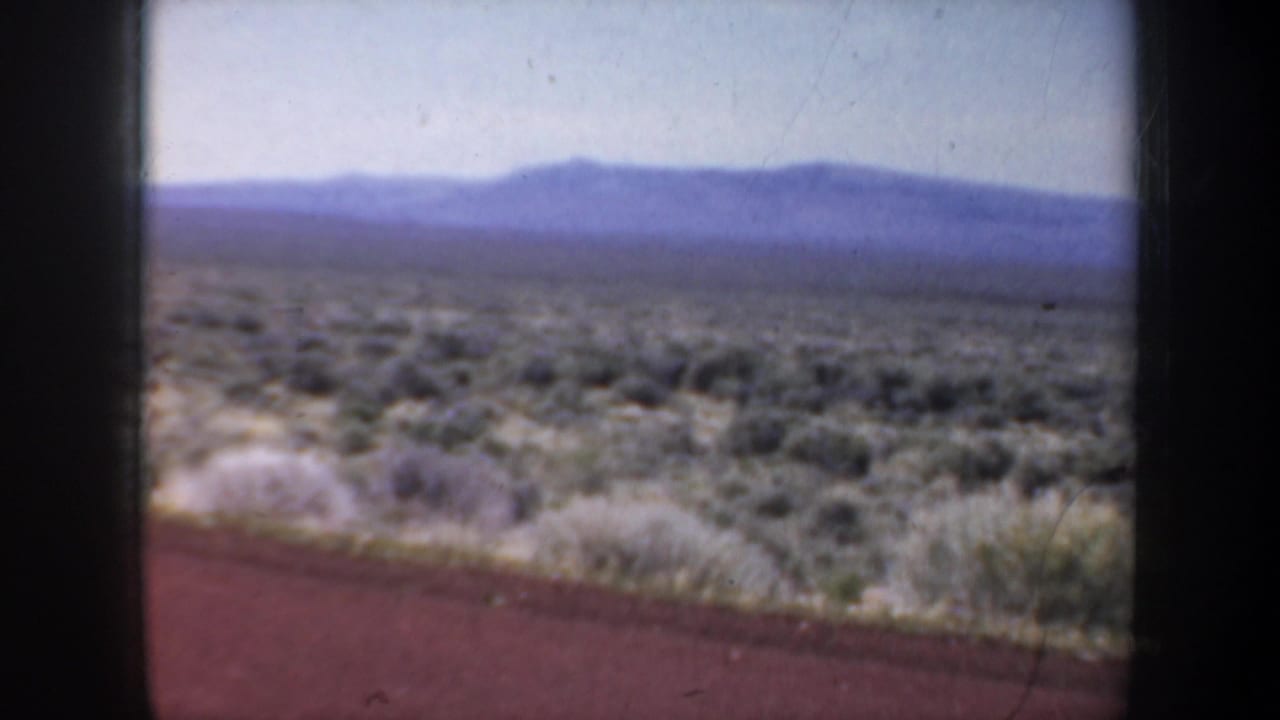 Open scrub plain and hazy mountain ridge beyond a reddish roadside strip.
