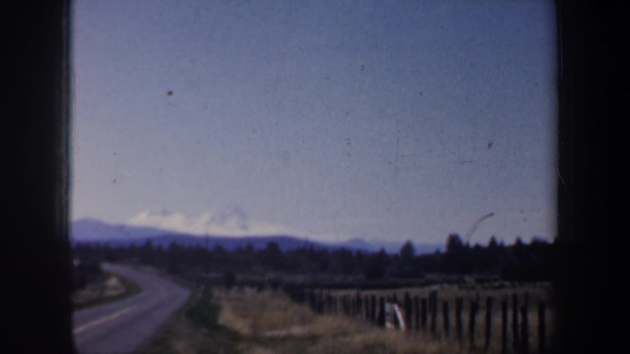 Rural road, fence line, fields, and hazy mountains seen through 8mm frame edges.
