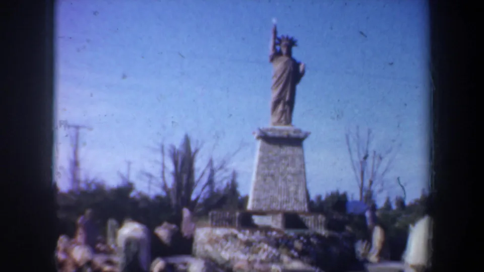 Oregon 1957 home-movie frame showing a distant statue on a pedestal with visitors gathered below.