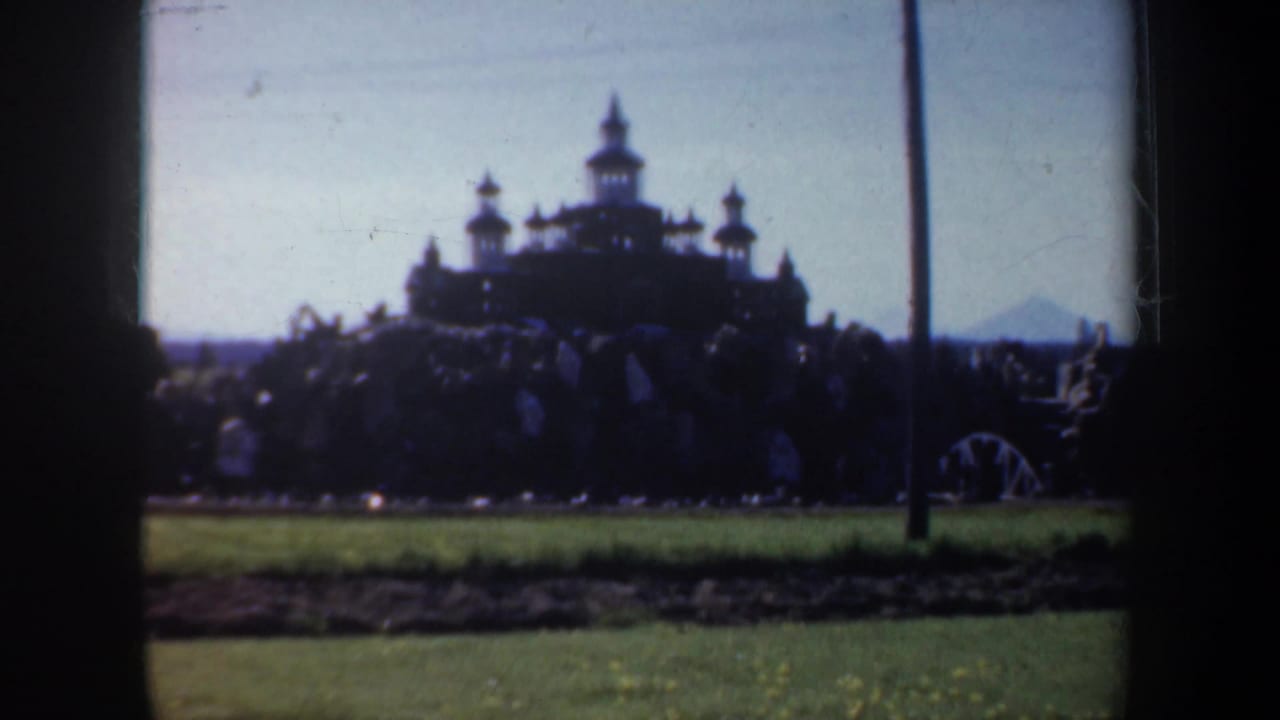 A distant castle-like building or miniature structure appears in silhouette across a grassy area in the Oregon home movie.