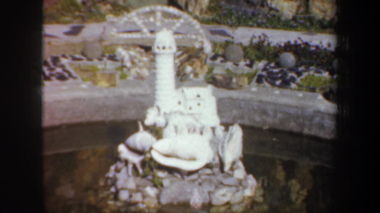 White lighthouse model beside a small pond with shells and rocks.