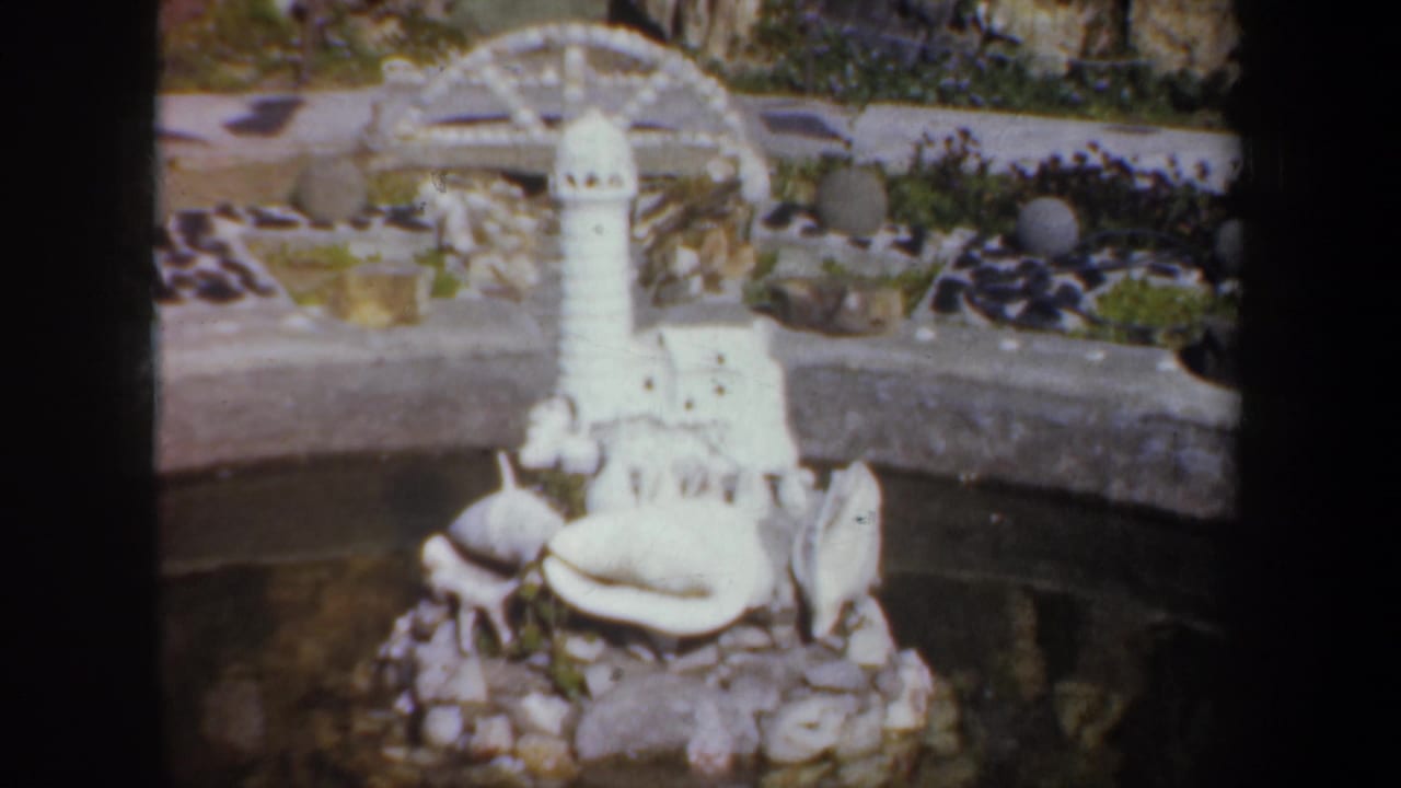 White lighthouse miniature and shell-covered pond edge in a rock garden.