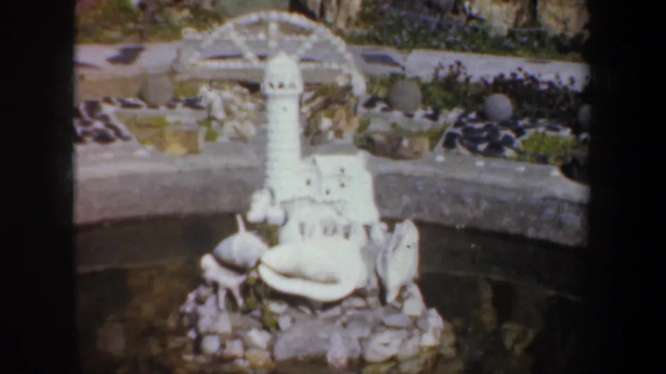 1957 Oregon frame with a white lighthouse miniature, shells, rocks, and a curved pond edge in a handmade garden scene.