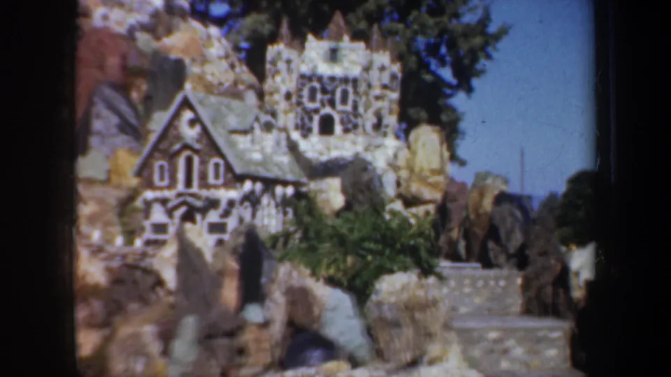 1957 Oregon frame showing a castle-like stone miniature with steps, pebble walls, rocks, and greenery in the garden display.
