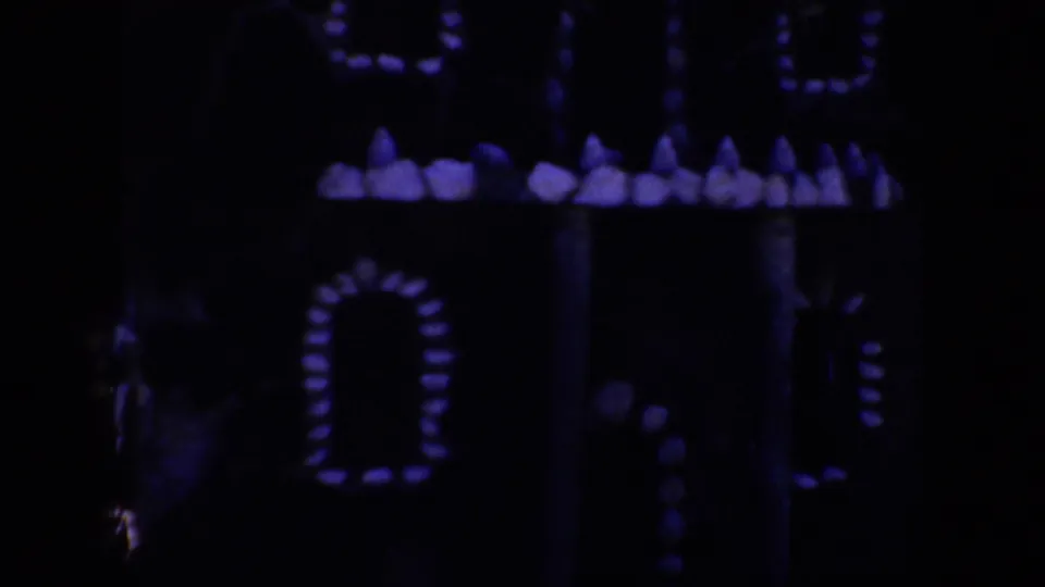 1957 Oregon 8mm frame showing a dark house or model-like facade with purple glowing window patterns and deep shadow.