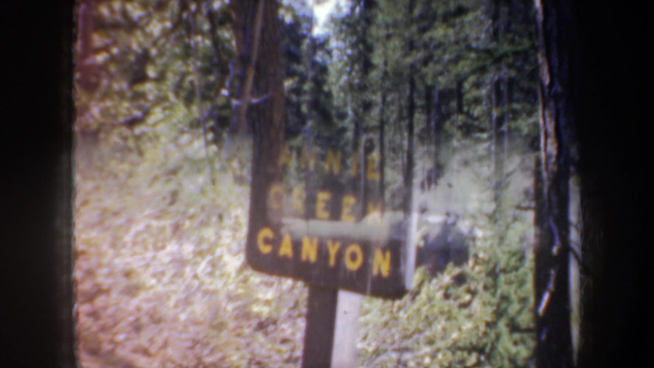 1957 Oregon home-movie frame with an Annie Creek Canyon sign partly softened by light and forest foliage.