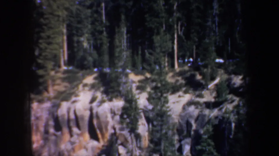 1957 Oregon home-movie view of a tan and ochre rocky slope bordered by dense evergreen forest.