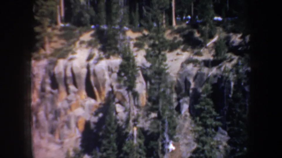 Vintage Oregon 8mm frame with tan rock faces, scattered evergreens, and deep forest shade.