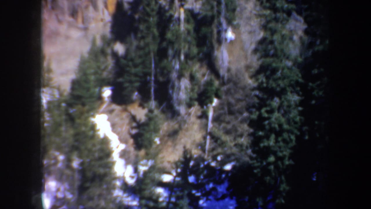 Elevated 1957 Oregon view of a forested cliffside with bright snow traces among evergreens and rock.