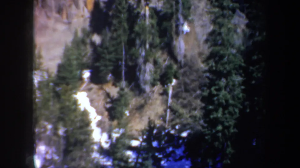 Elevated 1957 Oregon view of a forested cliffside with bright snow traces among evergreens and rock.