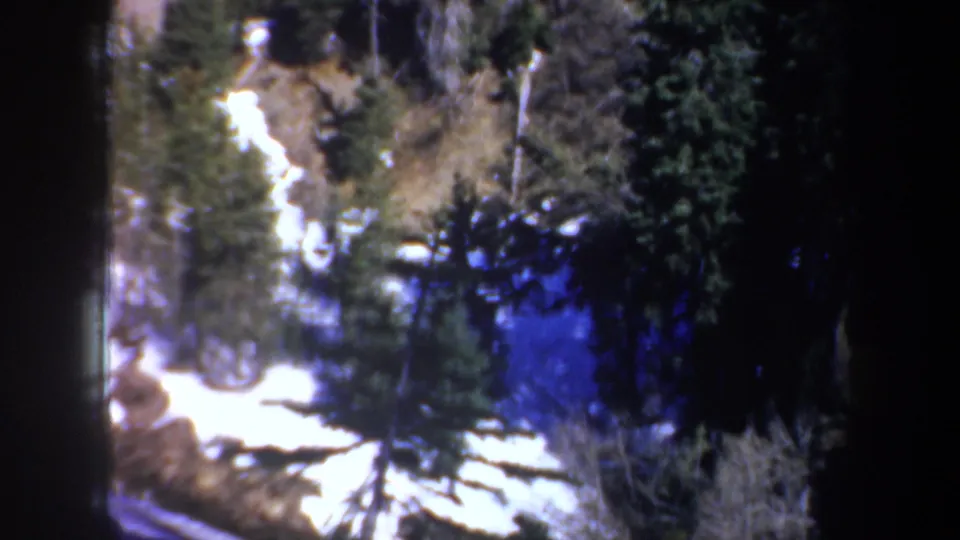 Oregon 8mm home-movie frame with snow on a lower slope, evergreens, and dark forest shadow.