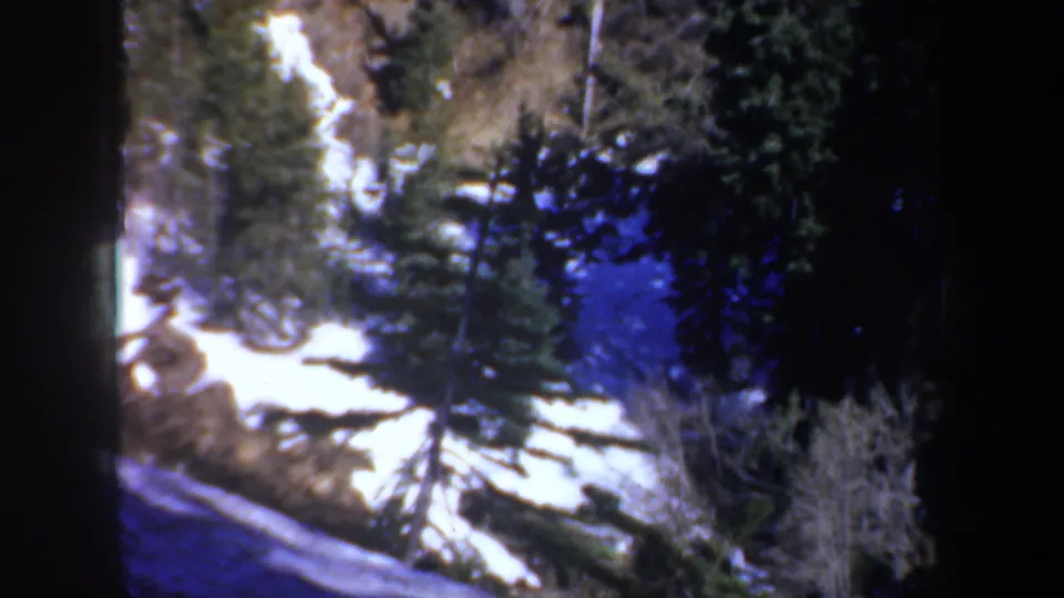 1957 Oregon elevated landscape view with conifers, snow patches, and rough hillside terrain on 8mm film.