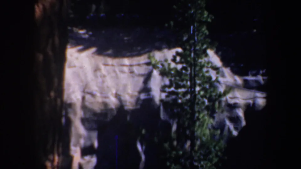 Oregon forest frame from 1957 8mm footage, showing a pale rocky outcrop partly framed by dark pine trees.