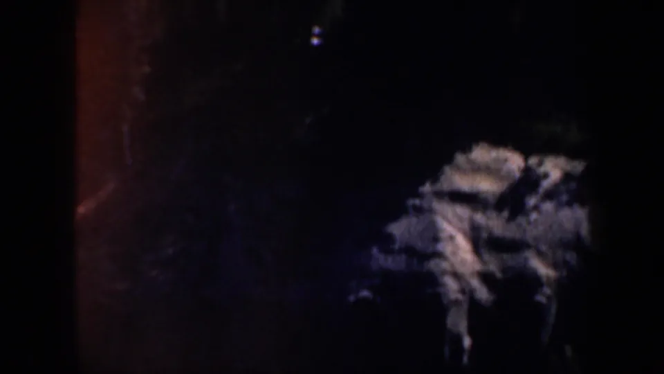 1957 Oregon 8mm frame showing a dim rocky night landscape with scattered faint light and heavy shadow.