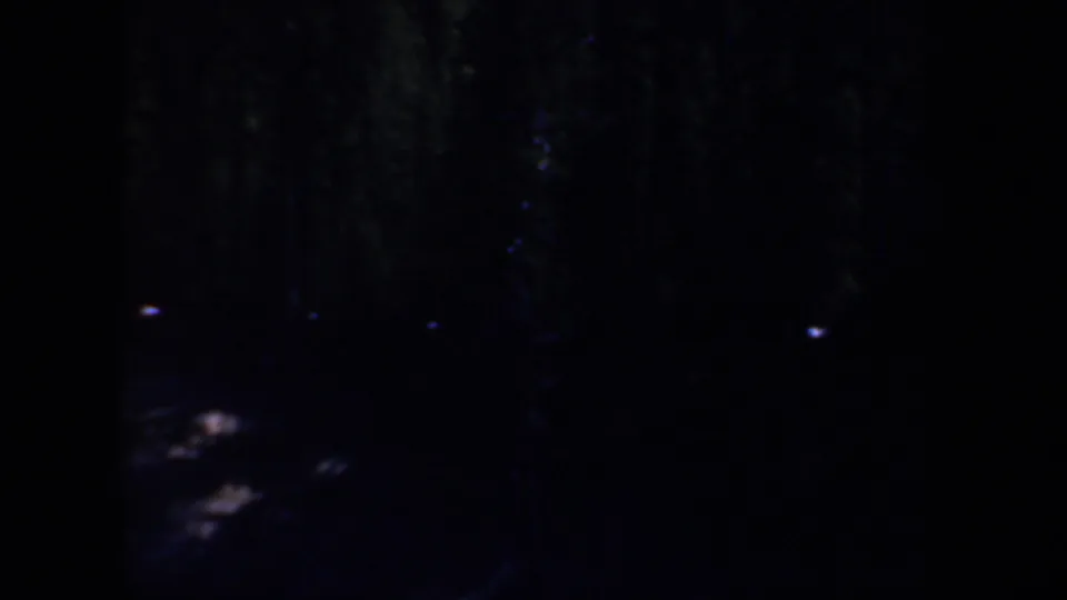 1957 Oregon 8mm frame showing an underexposed outdoor night view with faint lights and indistinct rocky ground.