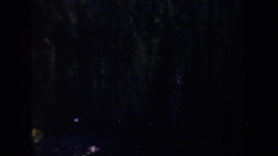 1957 Oregon 8mm frame showing a dim night landscape with a pale rocky form at upper right and deep shadow below.