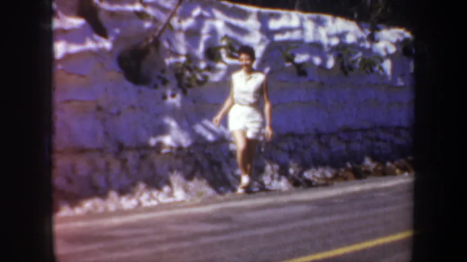 The woman steps along the roadside in white shorts, filmed in soft, faded 8mm color during an Oregon trip.