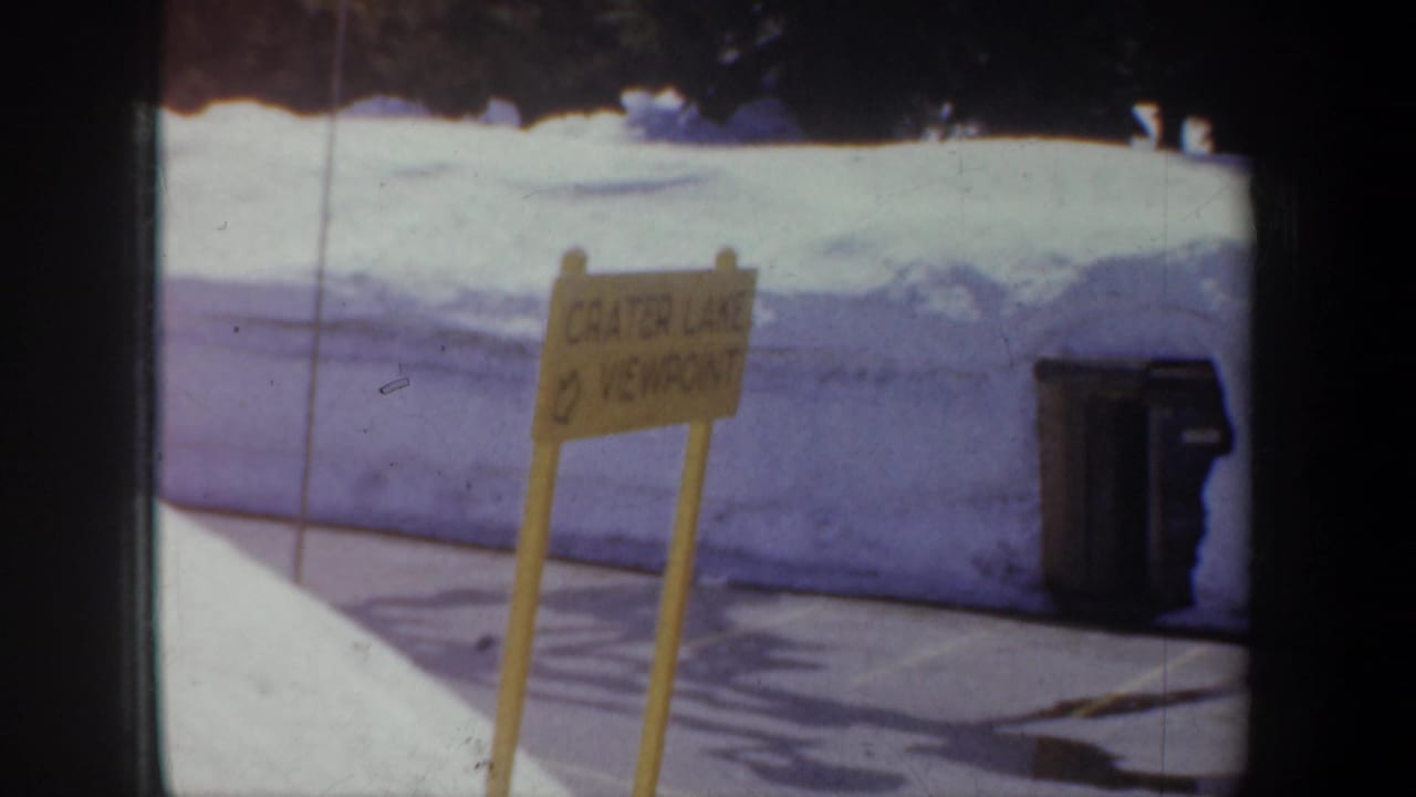 Yellow Crater Lake viewpoint sign beside snowbanks and bins.