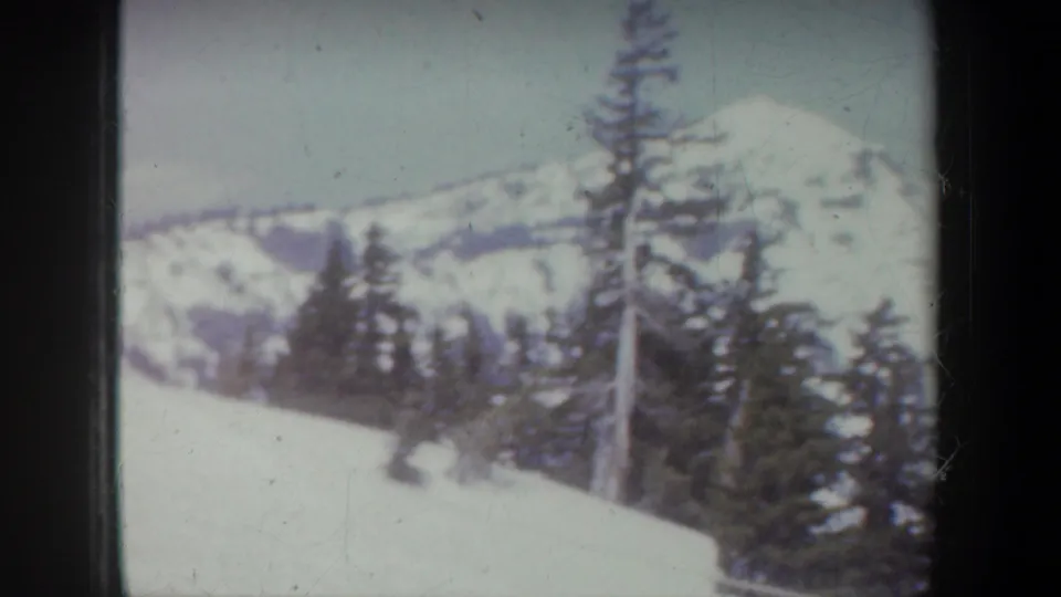 1957 Oregon 8mm frame looking across snowy evergreens toward a bright mountain ridge.