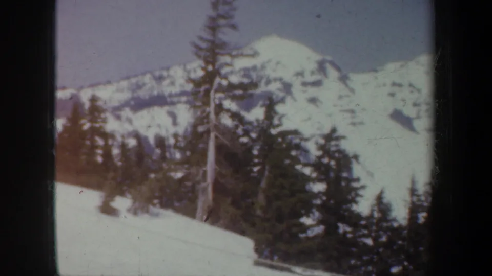 1957 Oregon home-movie frame of snow-covered mountains and evergreen forest in winter light.